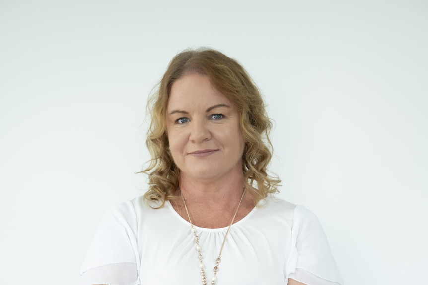 A woman with shoulder-length curly hair and a white shirt smiles.