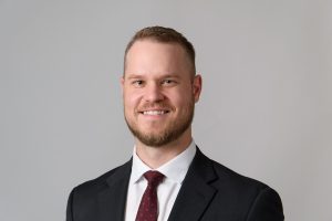 Nick Kuhlman, wearing a tie and suit jacket, smiles for the camera